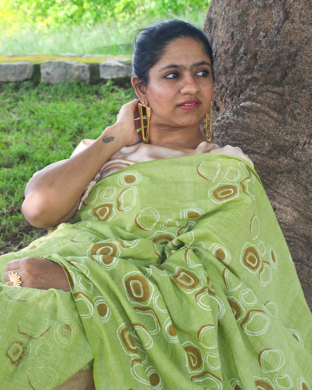 Woman wearing green saree and resting on tree