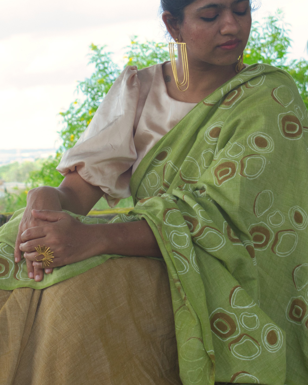 Woman in green and brown saree with off-whtite blouse and gold earrings