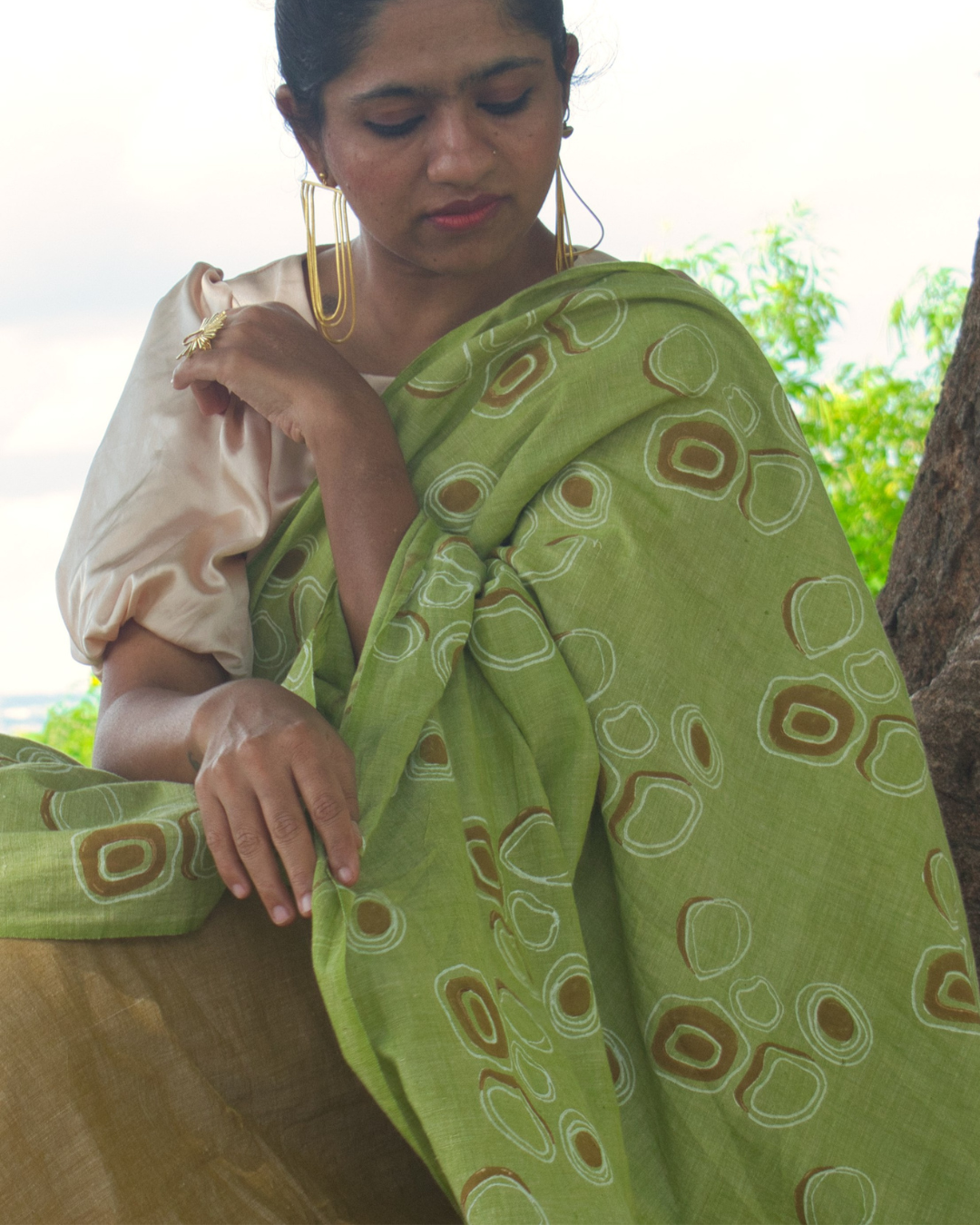 Woman fixing her palu in green and brown saree with gold earrings 
