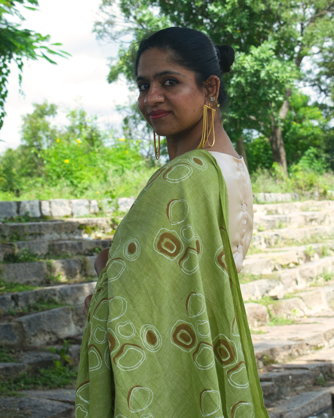 Woman showing her side profile in green hand block printed saree with  large gold earrings 