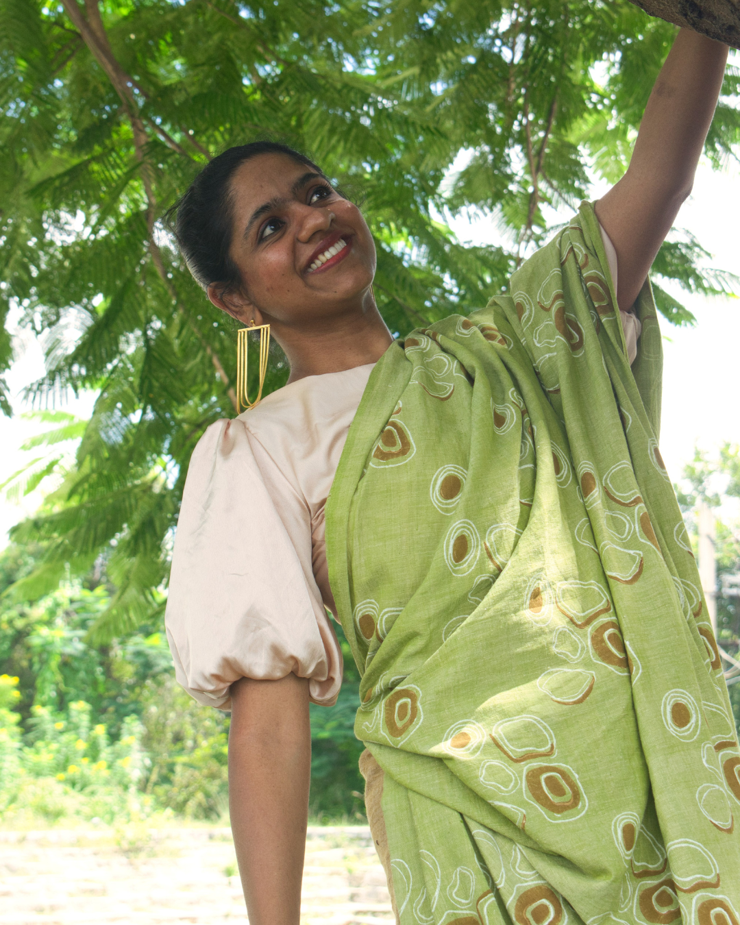 Woman hanging from a tree in a Green saree and puff sleeved off-white blouse 