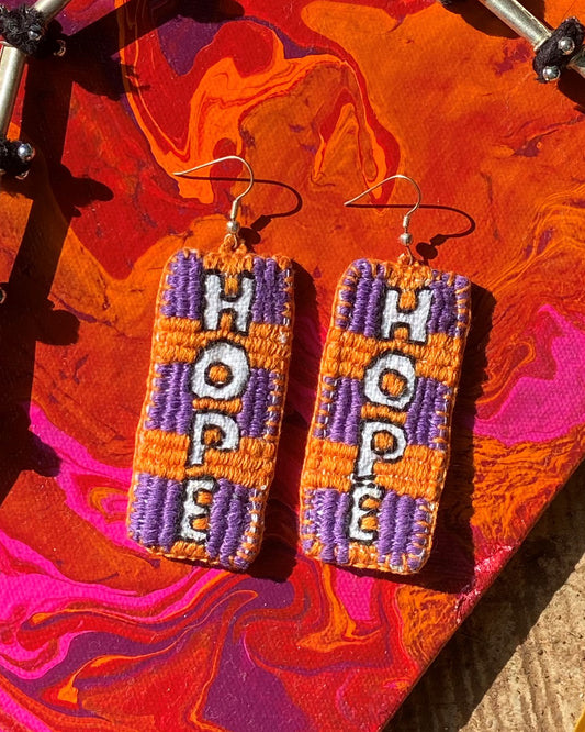 Hand embroidered purple and orange hook earrings on a marbled red pink and purple background 