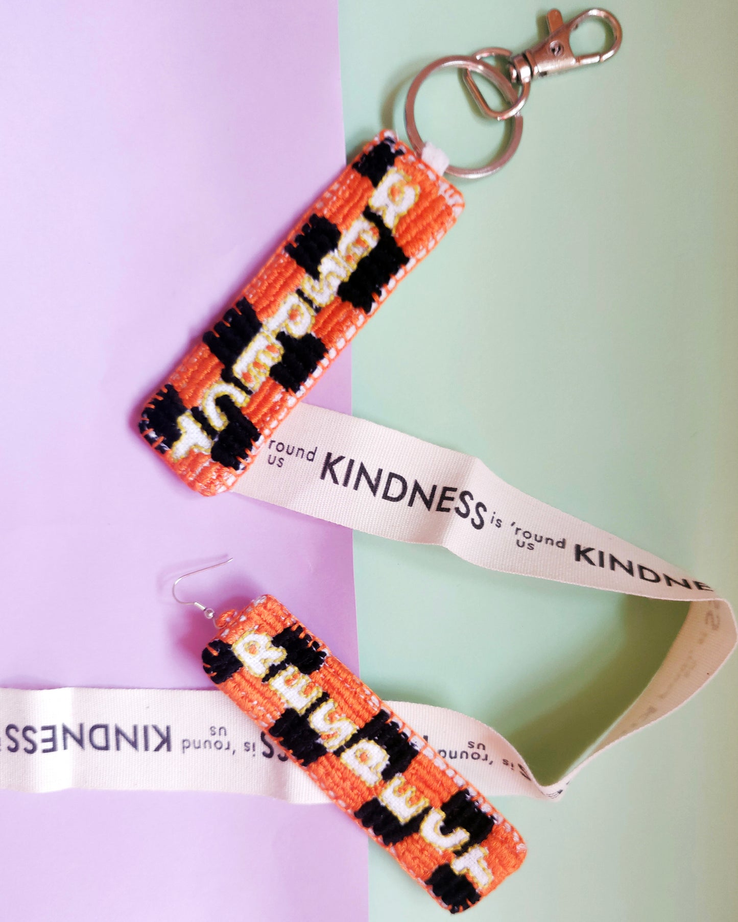 Hand embroidered earring and key chain on a purple and green background with Kindness tape 